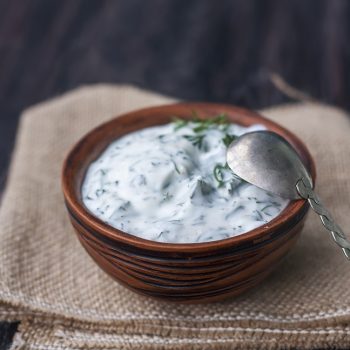 Bowl of fresh yogurt dip with dill and garlic on wooden background. selective Focus