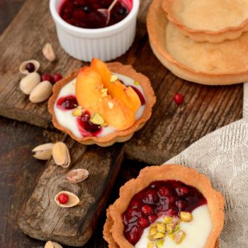 tartlets with cream berry sauce and pistachios on a wooden table with a linen napkin